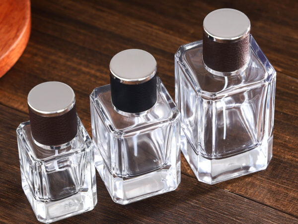Clear square glass perfume bottles with brown and black embossed leather caps and metallic sprayers