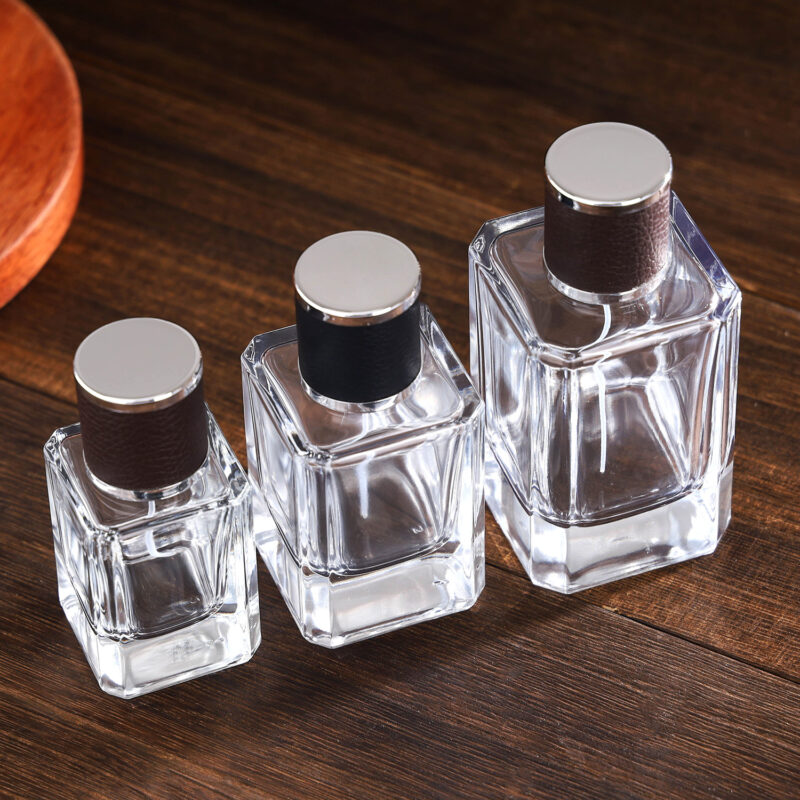 Clear square glass perfume bottles with brown and black embossed leather caps and metallic sprayers