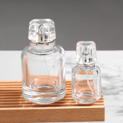 Transparent glass perfume bottle with a canister-style design, featuring a transparent acrylic cap and gold or silver spray nozzle