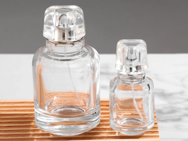 Transparent glass perfume bottle with a canister-style design, featuring a transparent acrylic cap and gold or silver spray nozzle